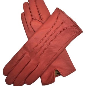 May include: A pair of red leather gloves with a stitched design on the back of the hand. The gloves are made of soft, supple leather and have a classic look.