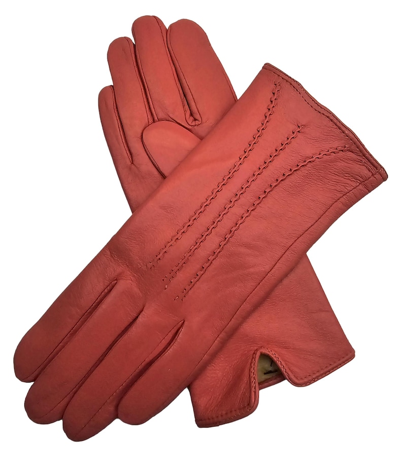 May include: A pair of red leather gloves with a stitched design on the back of the hand. The gloves are made of soft, supple leather and have a classic look.