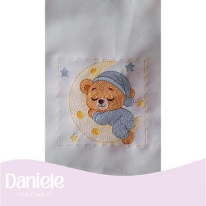May include: Embroidered patch featuring a sleeping teddy bear wearing a blue nightcap and pajamas, resting on a yellow crescent moon. The design includes yellow stars and is set against a white background. The text "Daniele Embroidery" is at the bottom.