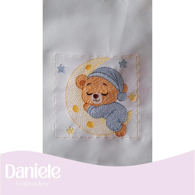 May include: Embroidered patch featuring a sleeping teddy bear wearing a blue nightcap and pajamas, resting on a yellow crescent moon. The design includes yellow stars and is set against a white background. The text "Daniele Embroidery" is at the bottom.