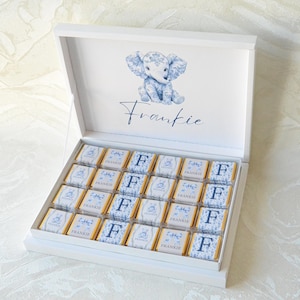 May include: A white rectangular gift box containing twenty-four individually wrapped chocolate squares. The inside lid features a blue floral elephant illustration and the name Frankie. Each chocolate wrapper displays either the name Frankie or the letter F.