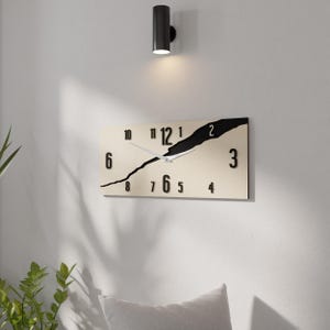 May include: A modern wall clock with a black and white design. The clock face is divided diagonally, with the top half black and the bottom half white. The numbers 1 through 12 are displayed in black on the white background, and the numbers 6, 7, 8, and 9 are displayed in black on the black background.