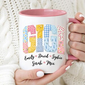 May include: White ceramic mug with a pink interior and handle. The word "GIGI" is displayed in colorful patchwork letters. Below the name are the names Emily, David, Sophie, Sarah, and Mia.