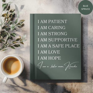 Peut inclure: Un journal vert-bleu avec du texte blanc qui dit "I AM PATIENT, I AM CARING, I AM STRONG, I AM SUPPORTIVE, I AM A SAFE PLACE, I AM LOVE, I AM HOPE." Un café et de la verdure sont à côté du journal.