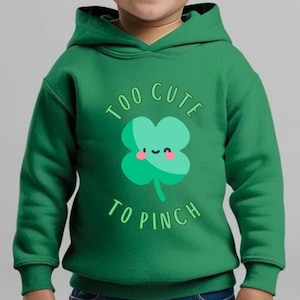 以下が含まれることがあります： 「Too Cute To Pinch」というテキストと、かわいい漫画のクローバーが描かれた緑色のパーカーです。