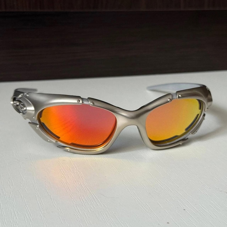 Puede incluir: Gafas de sol con montura plateada y lentes degradadas rojas y naranjas. Las gafas de sol tienen un dise&ntilde;o deportivo envolvente con un acabado met&aacute;lico. Las lentes hacen la transici&oacute;n de rojo a naranja.