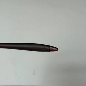 May include: A dark brown stylus with a rounded tip. The stylus is designed for use with a touchscreen device. The tip is a lighter shade of brown than the body of the stylus.