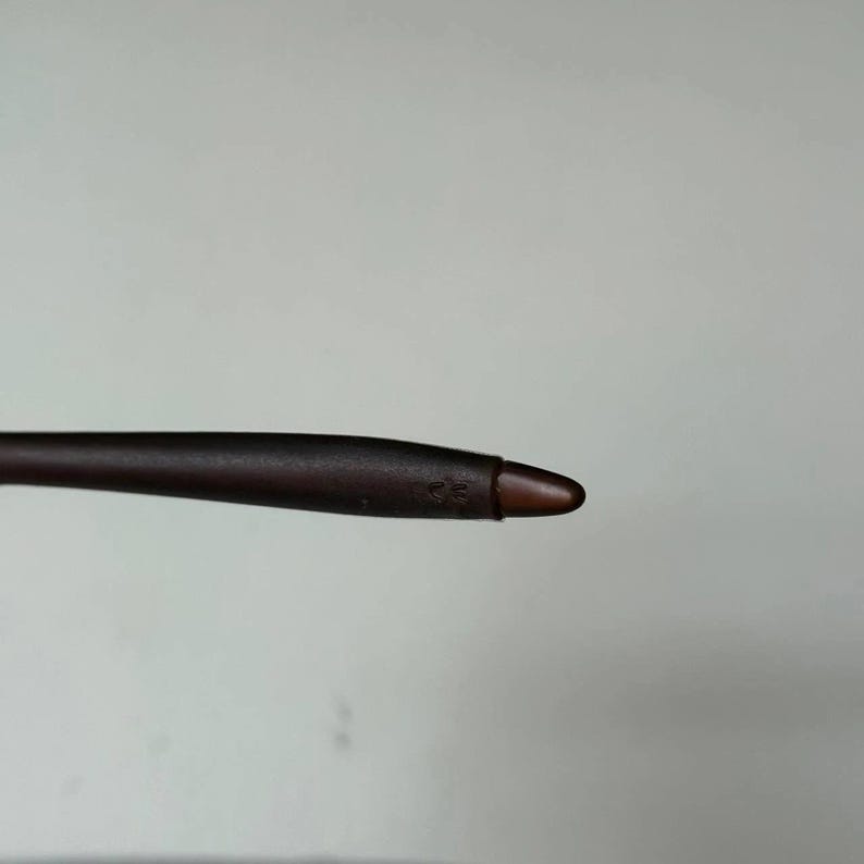 May include: A dark brown stylus with a rounded tip. The stylus is designed for use with a touchscreen device. The tip is a lighter shade of brown than the body of the stylus.