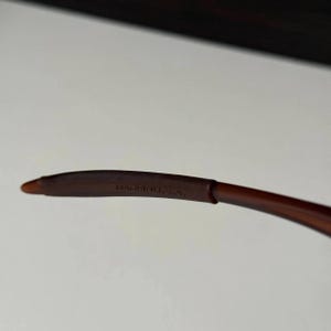 May include: Close-up of a brown eyeglass arm with the text "MADE IN U.S.A." printed in white. The arm is curved and has a smooth, matte finish.