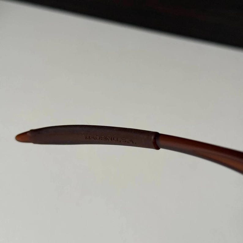 May include: Close-up of a brown eyeglass arm with the text "MADE IN U.S.A." printed in white. The arm is curved and has a smooth, matte finish.