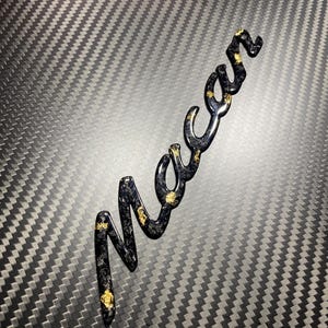 May include: Black and gold "Macan" logo with a carbon fiber background.