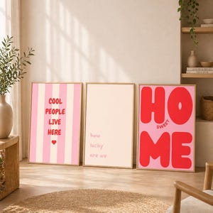 Könnte beinhalten: Drei gerahmte Kunstdrucke mit inspirierenden Zitaten. Einer mit rosa und weißen Streifen liest sich "COOL PEOPLE LIVE HERE" mit einem Herz. Ein anderer sagt "how lucky are we". Der dritte sagt "HOME SWEET ME".