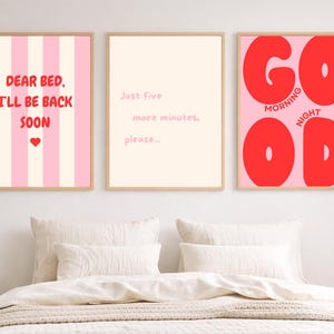 Op de afbeelding: Drie ingelijste wandposters met licht houten lijsten. De linker poster heeft roze en witte verticale strepen met de rode tekst "DEAR BED, I'LL BE BACK SOON" en een hartje. De middelste poster is cr&egrave;me met de tekst "Just five more minutes, please...". De rechter poster is roze met de grote rode tekst "GOOD MORNING NIGHT".