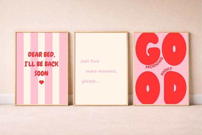 Op de afbeelding: Drie rechthoekige wandposters in lichte houten lijsten. De linker poster heeft roze strepen en de tekst "DEAR BED, I'LL BE BACK SOON" met een rood hartje. De middelste poster is cr&egrave;me met "Just five more minutes, please...". De rechter poster is roze met grote rode "GOOD" tekst en "MORNING" en "NIGHT" in kleinere rode letters.