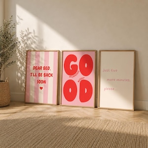 Op de afbeelding: Drie rechthoekige wandposters in houten lijsten. De eerste heeft roze strepen en de tekst 'DEAR BED, I'LL BE BACK SOON' met een hartje. De tweede heeft grote rode letters 'GOOD' en 'MORNING NIGHT'. De derde bevat de tekst 'Just five more minutes, please...'.