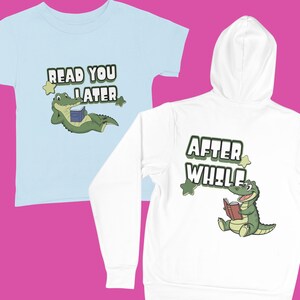 Könnte beinhalten: Hellblaues T-Shirt mit dem Text "READ YOU LATER" und einem Cartoon-Alligator, der ein Buch liest. Ein weißer Kapuzenpullover mit dem Text "AFTER WHILE" und einem Cartoon-Alligator, der ein Buch liest.