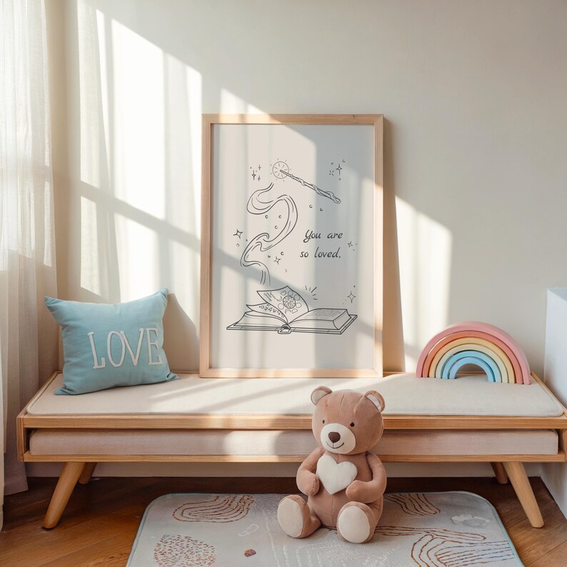 May include: A framed print with a whimsical illustration of a book and a wand, with the text "You are so loved." A light blue pillow with the word "LOVE" sits on a wooden bench. A teddy bear and a rainbow-shaped wooden toy are also present.