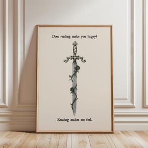 Peut inclure: Une affiche murale rectangulaire dans un cadre en bois clair présentant une illustration centrale d'une épée argentée entrelacée de vignes sombres et de roses. Le texte "Does reading make you happy?" figure au-dessus et "Reading makes me feel." en dessous.
