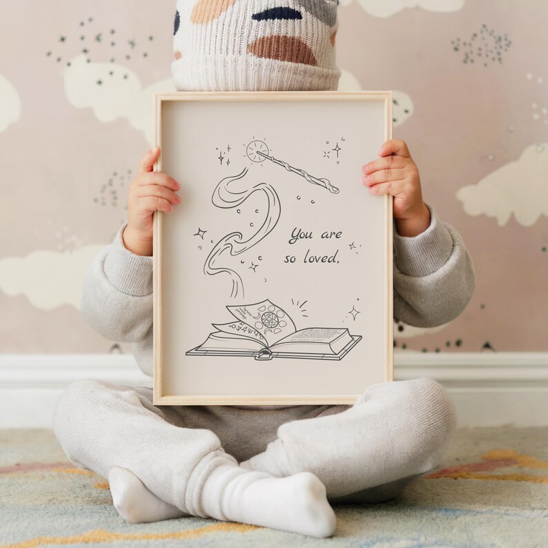 May include: A framed print with a whimsical illustration of a wand, smoke, and an open book. The text "You are so loved" is written in a delicate script. The frame is light-colored wood.