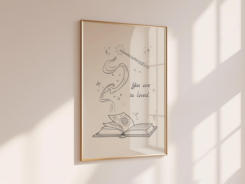 May include: A framed art print featuring a whimsical illustration. The artwork depicts an open book with a swirling design, a wand, and the text "You are so loved." The image is in black and white with a gold frame.