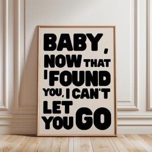 Könnte beinhalten: Ein rechteckiger Wandkunstdruck in einem hellen Holzrahmen mit fetter, serifenloser schwarzer Typografie auf cremefarbenem Hintergrund. Der Text lautet: BABY, NOW THAT I FOUND YOU, I CAN'T LET YOU GO. Das Design ist mittig im Rahmen platziert.