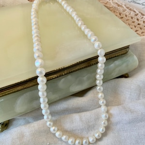 May include: A white pearl necklace with a silver clasp. The necklace is lying on a green and white marble surface.
