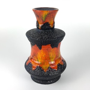 Puede incluir: Un jarrón de cerámica con base y cuerpo negros texturizados, con un vibrante esmalte naranja y amarillo que gotea por los lados. La parte superior del jarrón tiene forma acampanada con un esmalte similar.