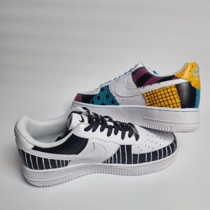 Puede incluir: Dos zapatillas blancas pintadas a medida. Una zapatilla presenta un dise&ntilde;o de patchwork con detalles turquesa, morado y amarillo. La otra zapatilla tiene un patr&oacute;n de rayas blancas y negras. Ambas zapatillas tienen suelas blancas y cordones negros.
