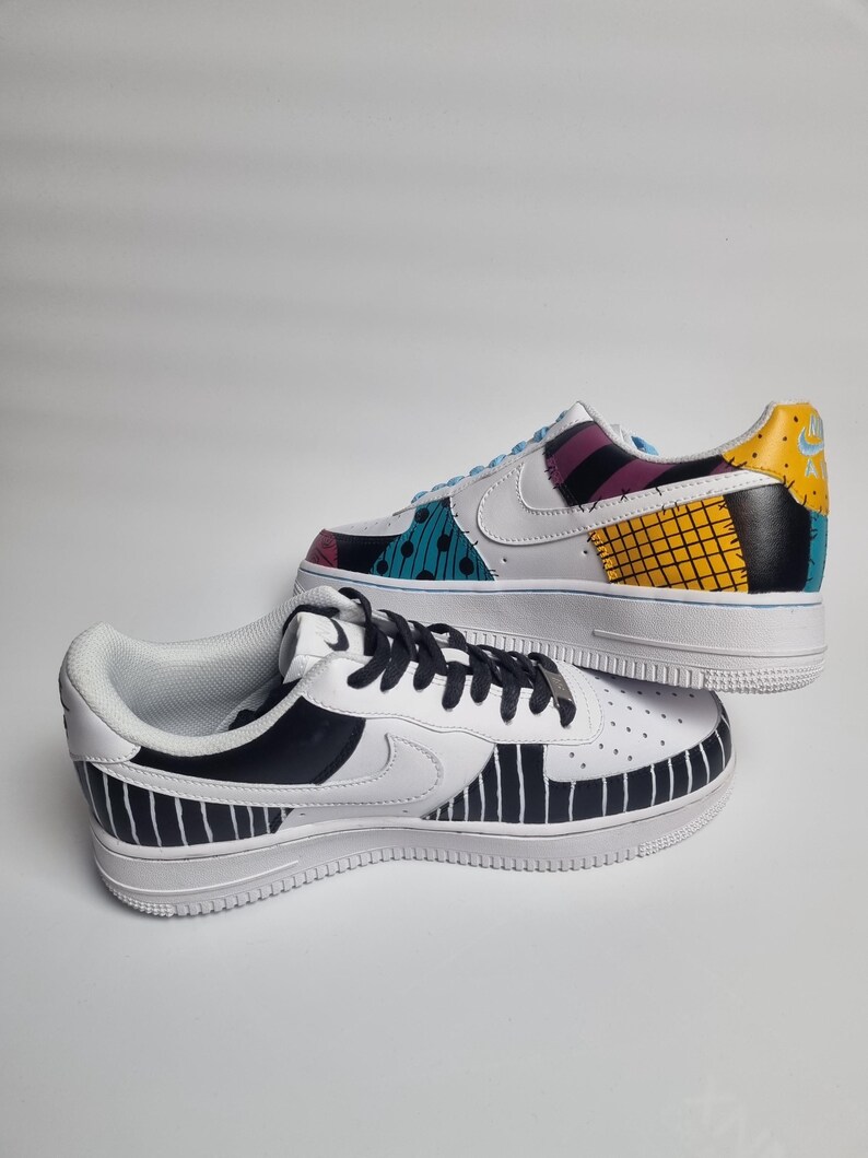 Puede incluir: Dos zapatillas blancas pintadas a medida. Una zapatilla presenta un dise&ntilde;o de patchwork con detalles turquesa, morado y amarillo. La otra zapatilla tiene un patr&oacute;n de rayas blancas y negras. Ambas zapatillas tienen suelas blancas y cordones negros.