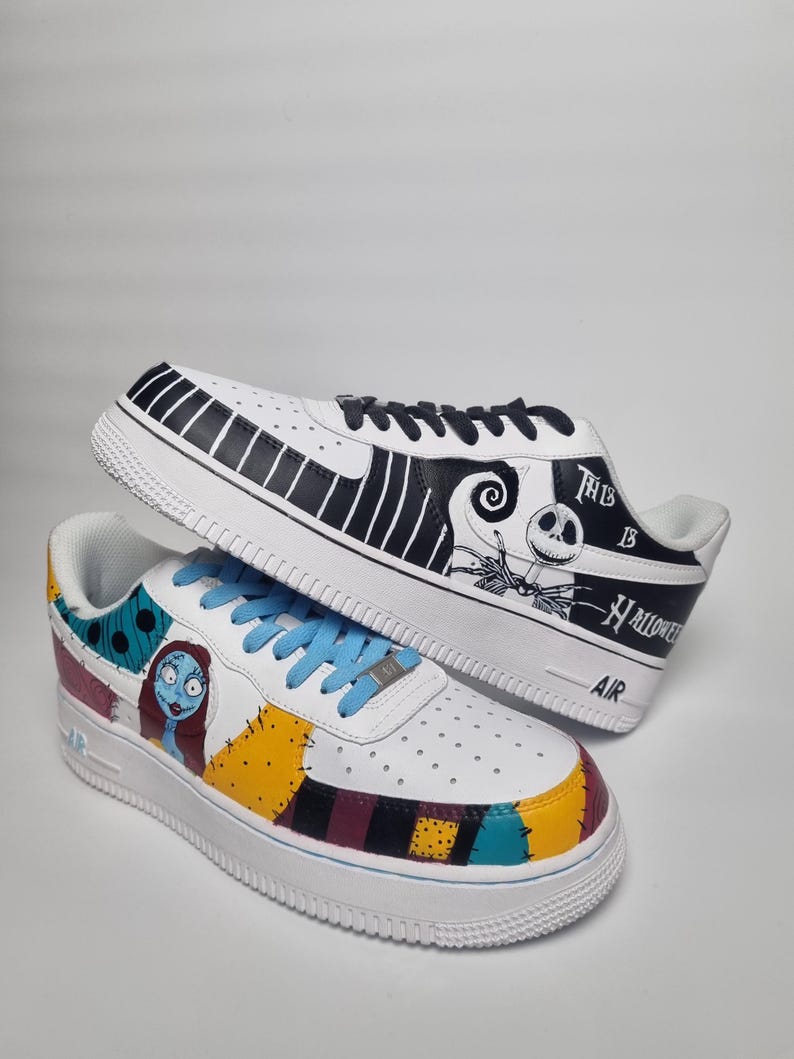Puede incluir: Un par de zapatillas blancas con ilustraciones personalizadas. Una zapatilla presenta un dise&ntilde;o en blanco y negro con el texto "This is Halloween". La otra tiene un dise&ntilde;o de patchwork colorido y una ilustraci&oacute;n de personaje. Cordones azules.