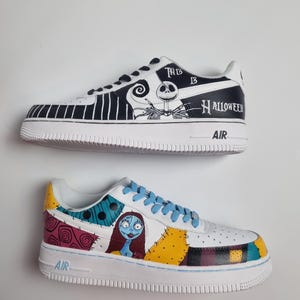 Puede incluir: Dos zapatillas pintadas a medida. Una presenta un dise&ntilde;o en blanco y negro con Jack Skellington y el texto "This is Halloween". La otra zapatilla tiene un dise&ntilde;o de patchwork con Sally de Pesadilla antes de Navidad.