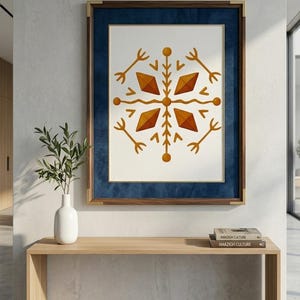 May include: A framed art print featuring a symmetrical geometric design in shades of orange and brown on a white background. The artwork is set within a blue velvet mat and a wooden frame with gold accents. The print is displayed above a wooden console table.