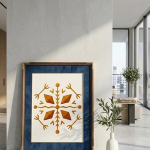 May include: A framed art print featuring a symmetrical, geometric design in shades of orange and gold on a cream background. The artwork is set within a dark blue mat and a wooden frame with gold accents, displayed in a modern interior setting.