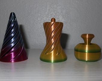 May include: Three 3D printed objects with a gradient color scheme. The objects are a cone, a vase, and a small round object with a knob on top. The cone is blue and purple, the vase is orange and green, and the round object is gold and green.