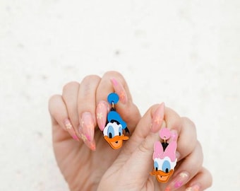 Ett par handgjorda örhängen med Kalle och Daisy-motiv i metakrylat och rostfritt stål