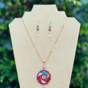 May include: A gold necklace with a colorful beaded pendant and matching earrings. The pendant is a circular design with red, white, turquoise, and gold beads.