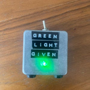 May include: A silver box with a green light on the front. The box has a toggle switch on the top and the words "GREEN LIGHT GIVEN" printed on the front.