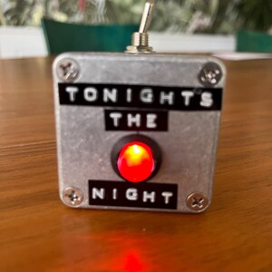 May include: A silver metal box with a red light and a toggle switch. The box has the words "Tonight's The Night" printed on it.