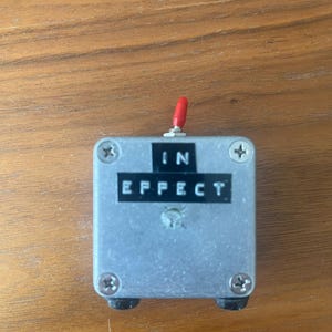 May include: A silver effect pedal with a red knob and the words "IN EFFECT" printed on the front.