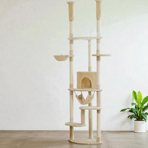 Op de afbeelding: Beige kattenboom met meerdere niveaus, inclusief een hangmat, een grot en verschillende platforms. Het hoge, verticale ontwerp heeft een neutrale kleurstelling en is geschikt voor gebruik binnenshuis. Een potplant is zichtbaar op de achtergrond.