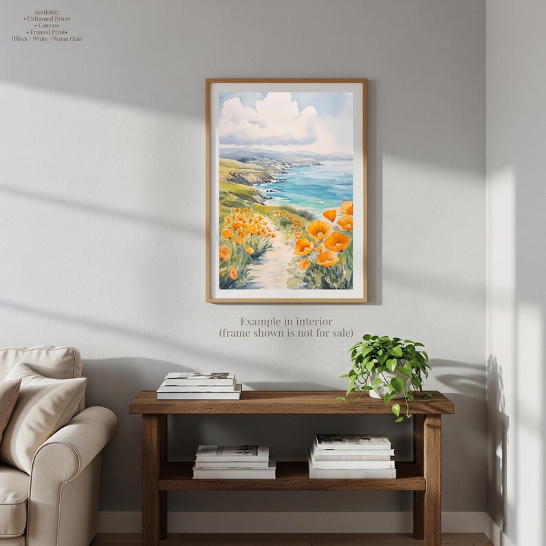a living room with a wooden console table, a white sofa, and a framed painting of a coastal landscape with orange flowers.