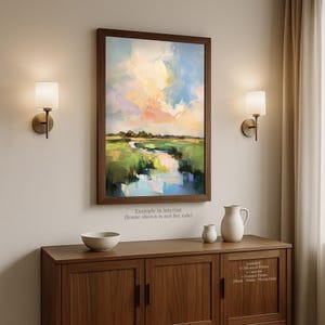 a large painting of a landscape hanging on a wall above a wooden cabinet with a white pitcher and a small white bowl on top.