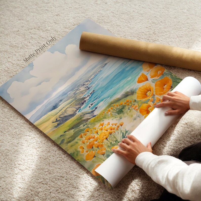 A person is holding a roll of paper and placing it on a painting of a landscape with a blue sky and orange flowers.