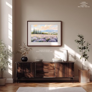 a wooden cabinet with a vase of flowers and a stack of books on top, set against a beige wall with a framed landscape painting hanging above it.