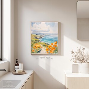 a bathroom with a framed painting of a coastal landscape hanging on the wall, depicting a beach with a blue sky and ocean.