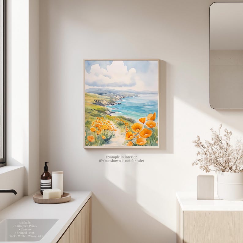 a bathroom with a framed painting of a coastal landscape hanging on the wall, depicting a beach with a blue sky and ocean.