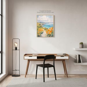 a serene workspace with a wooden desk, a black chair, and a painting of a coastal landscape with orange flowers hanging on the wall.