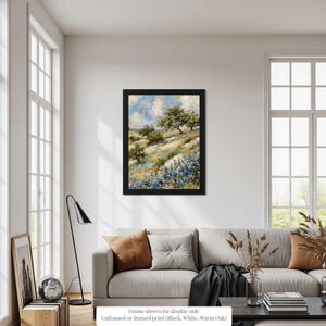 a living room with a large window, a gray sofa, a framed landscape painting hanging on the wall, and various decorative elements such as a vase and a plant.