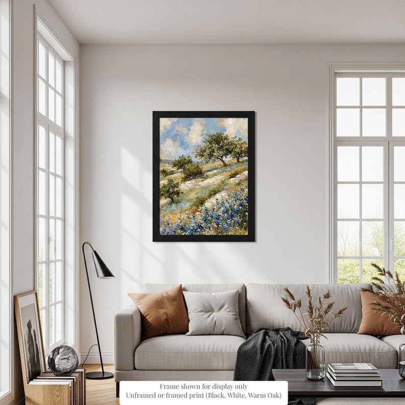 a living room with a large window, a gray sofa, a framed landscape painting hanging on the wall, and various decorative elements such as a vase and a plant.