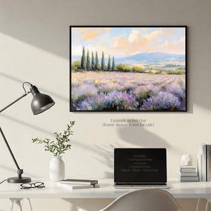 a painting of a field of lavender flowers hanging on a wall above a desk with a laptop, books, and a plant.